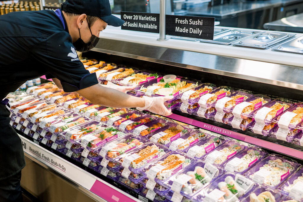 A worker placing pre-packaged sushi for display at a grocery store